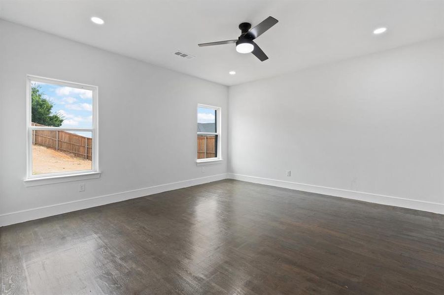 Unfurnished room featuring ceiling fan, dark wood-type flooring, and plenty of natural light