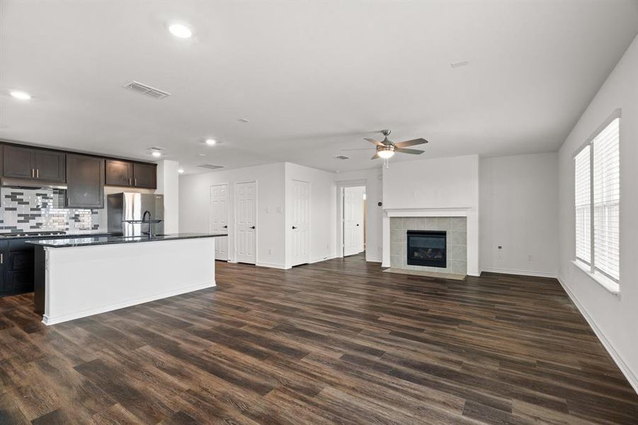 Kitchen with an island with sink, dark brown cabinetry, dark hardwood / wood-style floors, tasteful backsplash, and a fireplace