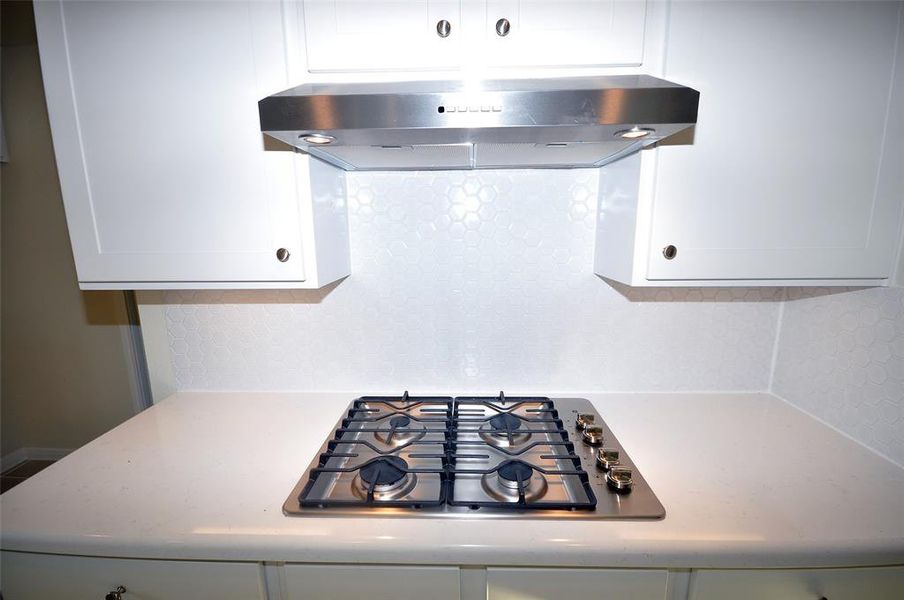 Natural gas cooktop under an externally vented hood.