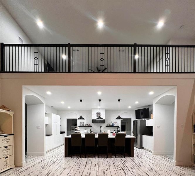 Kitchen with a large island with sink, tasteful backsplash, stainless steel refrigerator, light wood-type flooring, and a breakfast bar