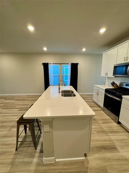 Kitchen with white cabinetry, light hardwood / wood-style flooring, stainless steel appliances, sink, and a center island with sink