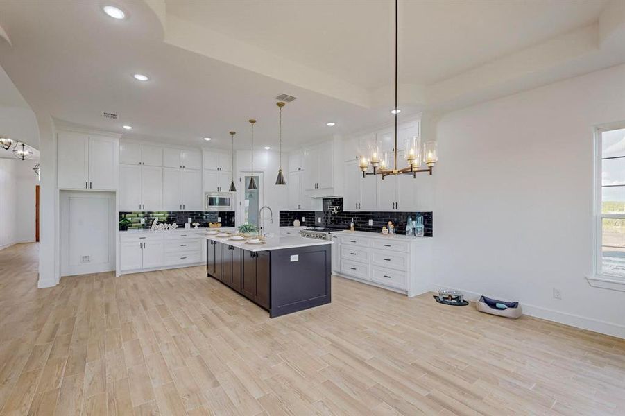 Kitchen with white cabinetry, pendant lighting, an island with sink, stainless steel microwave, and backsplash