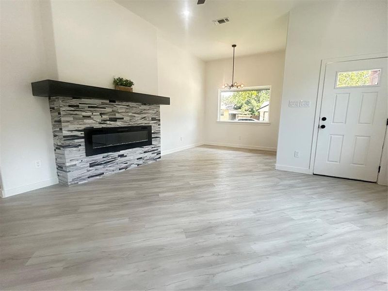 Unfurnished living room with a stone fireplace, a notable chandelier, light wood-type flooring, and a high ceiling