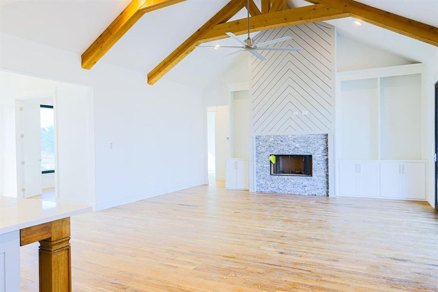 Unfurnished living room with beam ceiling, light hardwood / wood-style flooring, ceiling fan, a large fireplace, and high vaulted ceiling