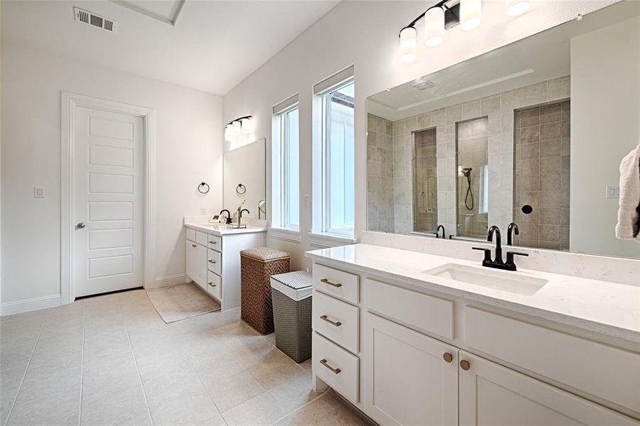 Bathroom with double vanity, tile patterned flooring, tiled shower, and plenty of natural light