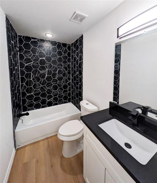 Full bathroom with tiled shower / bath combo, hardwood / wood-style flooring, vanity, and toilet