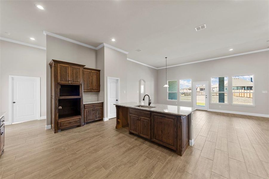 Kitchen with an island with sink, sink, light stone countertops, crown molding, and light hardwood / wood-style floors