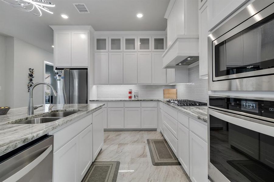 Kitchen featuring custom exhaust hood, tasteful backsplash, stainless steel appliances, white cabinets, and sink