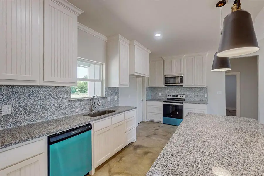 Kitchen with white cabinets, sink, light stone counters, appliances with stainless steel finishes, and backsplash