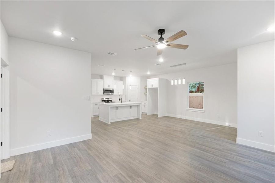 Unfurnished living room featuring light wood-type flooring, ceiling fan, and sink