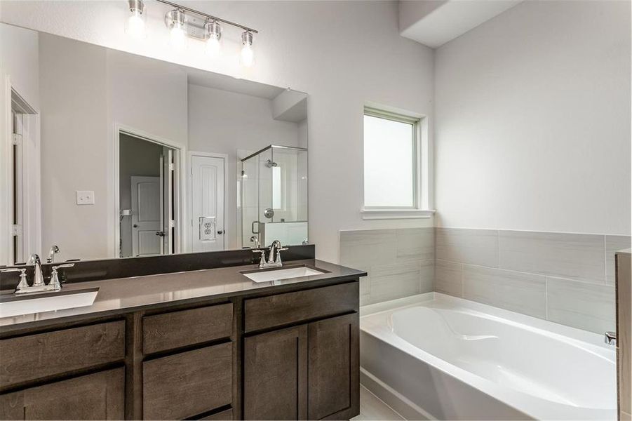 Indulge in the elegant primary bathroom with dual vanities, a large soaking tub, and a separate glass-enclosed shower. The modern fixtures and ample counter space provide both luxury and functionality. Photos are from another Rylan floor plan.