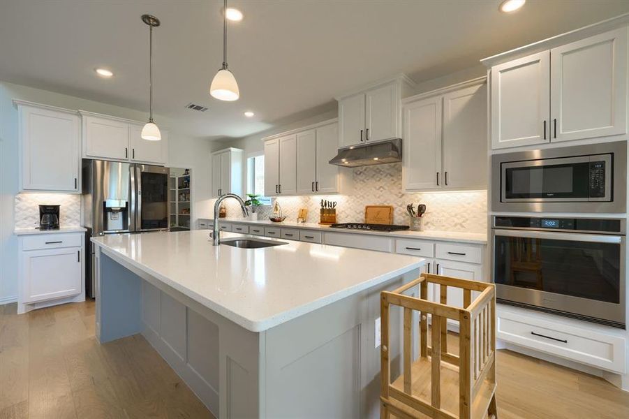 Kitchen with appliances with stainless steel finishes, sink, tasteful backsplash, and light hardwood / wood-style flooring