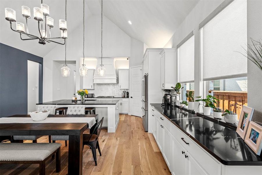 Kitchen with white cabinetry, light hardwood / wood-style floors, hanging light fixtures, premium range hood, and high vaulted ceiling