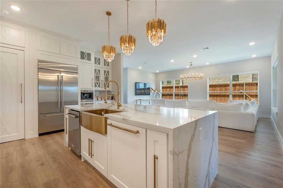 Kitchen featuring light hardwood / wood-style floors, stainless steel appliances, a kitchen island with sink, light stone countertops, and white cabinets