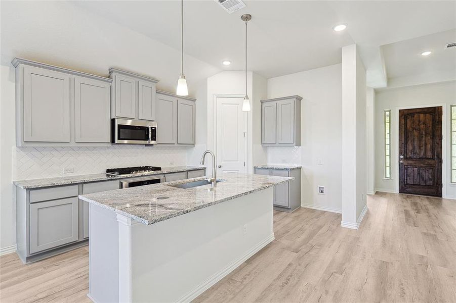 Kitchen with light stone counters, sink, light hardwood / wood-style flooring, appliances with stainless steel finishes, and vaulted ceiling