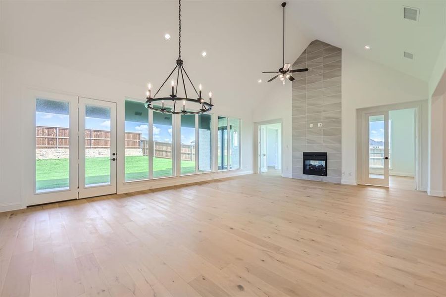 Unfurnished living room featuring a tiled fireplace, ceiling fan with notable chandelier, light hardwood / wood-style flooring, tile walls, and high vaulted ceiling