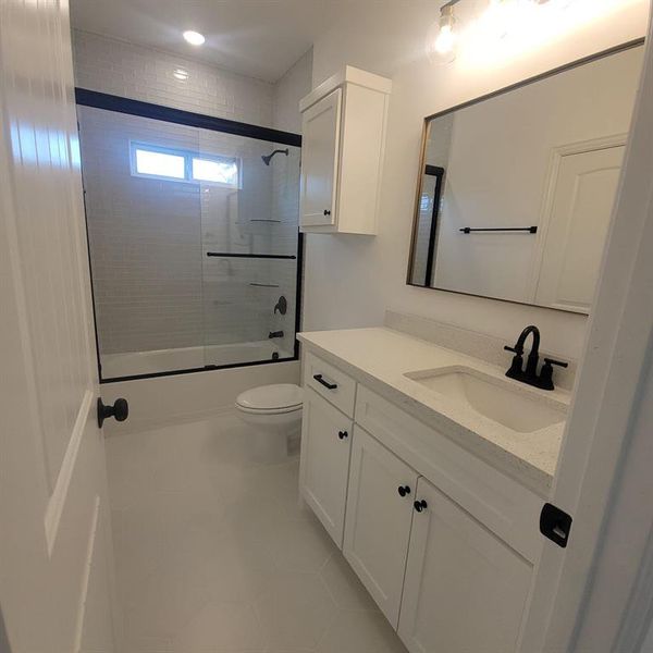Full bathroom featuring tile flooring, shower / bath combination with glass door, toilet, and vanity