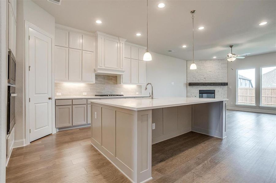 Kitchen featuring a fireplace, light hardwood / wood-style flooring, a center island with sink, decorative light fixtures, and ceiling fan