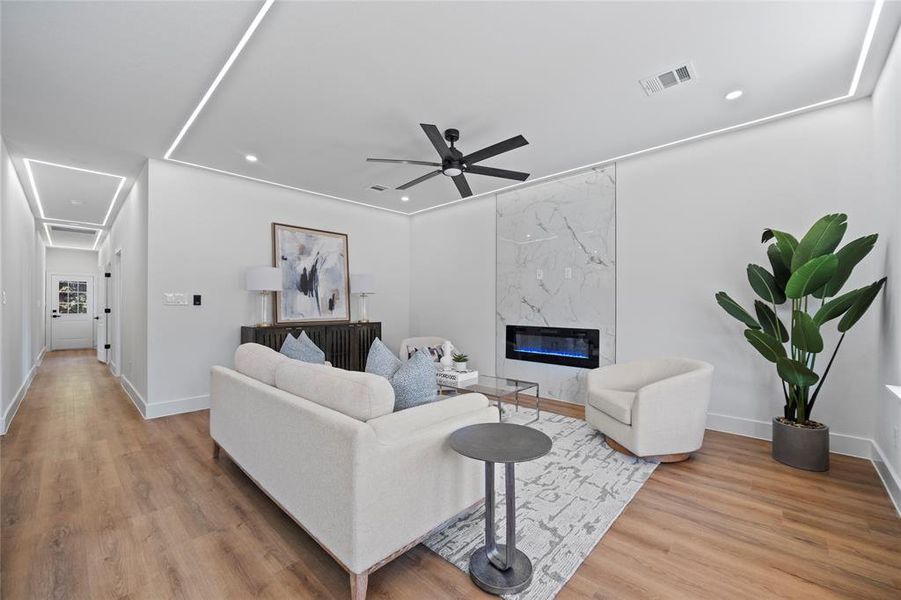 Living room with a high end fireplace, light hardwood / wood-style flooring, and ceiling fan