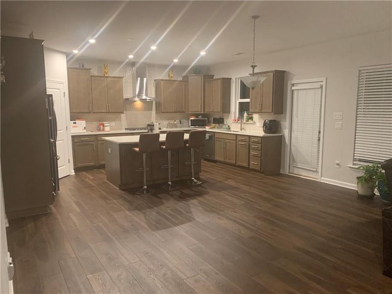 Kitchen featuring dark hardwood / wood-style flooring, wall chimney range hood, hanging light fixtures, a breakfast bar, and a kitchen island