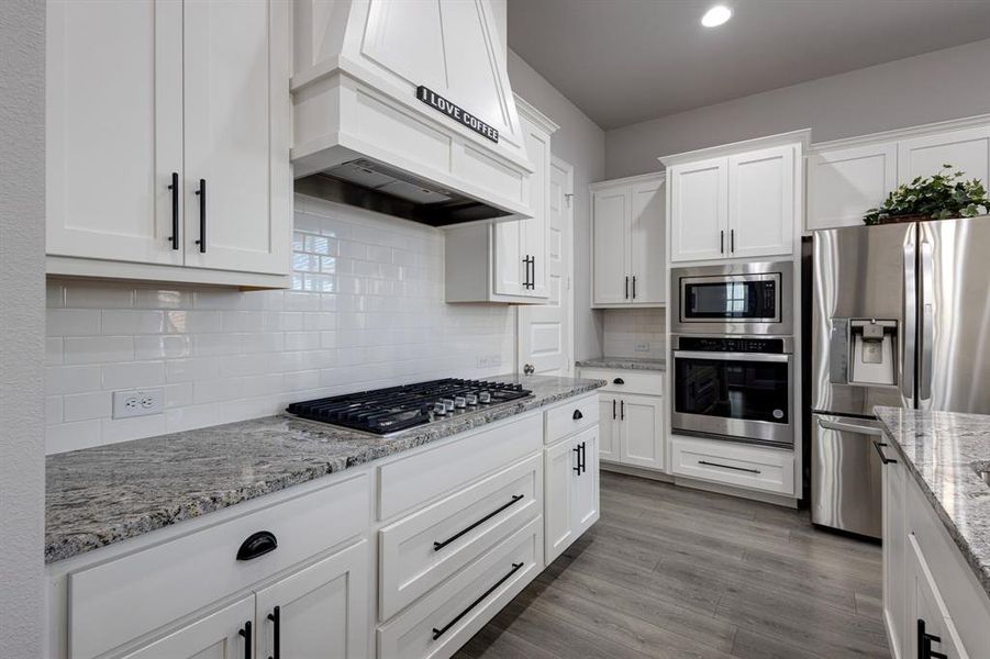 Kitchen with stainless steel appliances, hardwood / wood-style floors, custom range hood, and white cabinetry