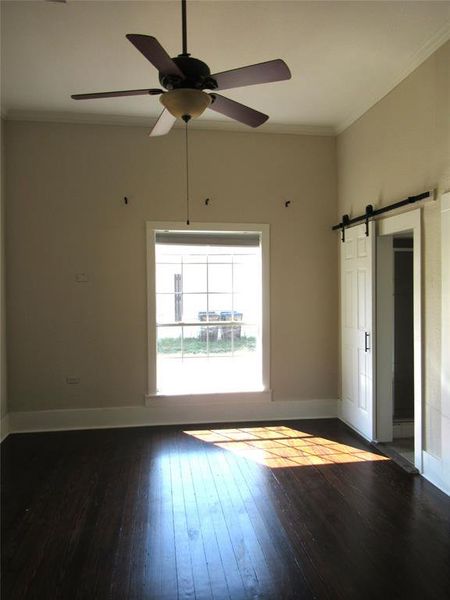 Spare room featuring dark wood-type flooring, crown molding, ceiling fan, and a barn door