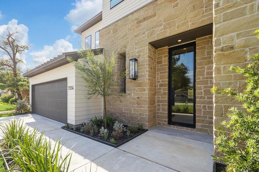 Modern two-story home featuring a stone facade, attached garage, and a sleek 10' steel front entry door, complemented by tasteful landscaping.