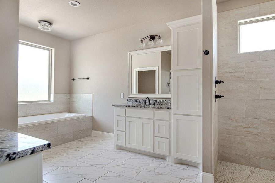 Bathroom featuring vanity, tile patterned flooring, and tiled bath