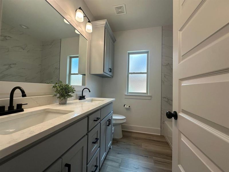 Full bathroom featuring tiled shower / bath combo, toilet, and viyln floors
