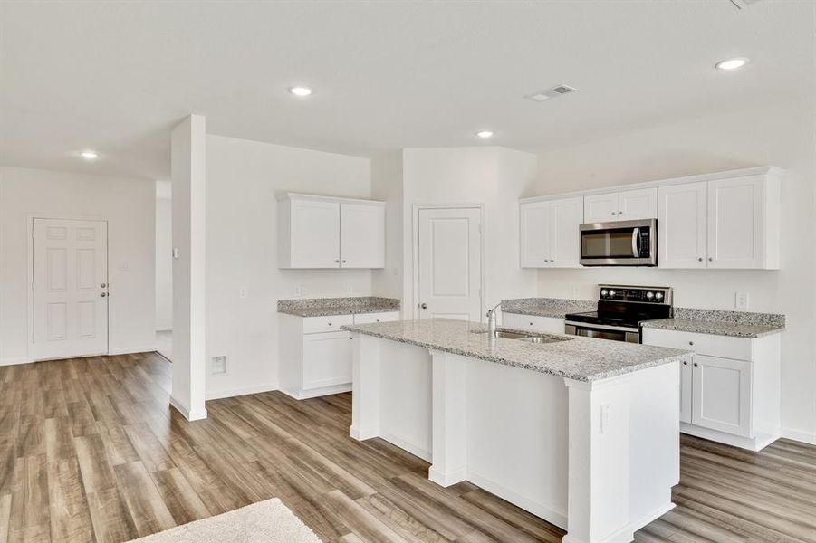 Kitchen featuring an island with sink, white cabinets, appliances with stainless steel finishes, and light wood-type flooring