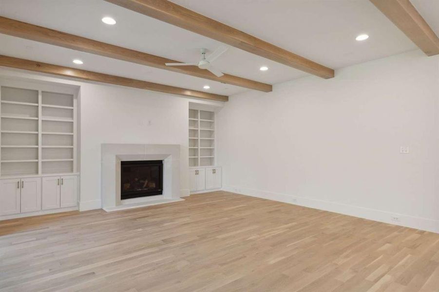 Unfurnished living room featuring beamed ceiling, ceiling fan, built in features, and light hardwood / wood-style flooring