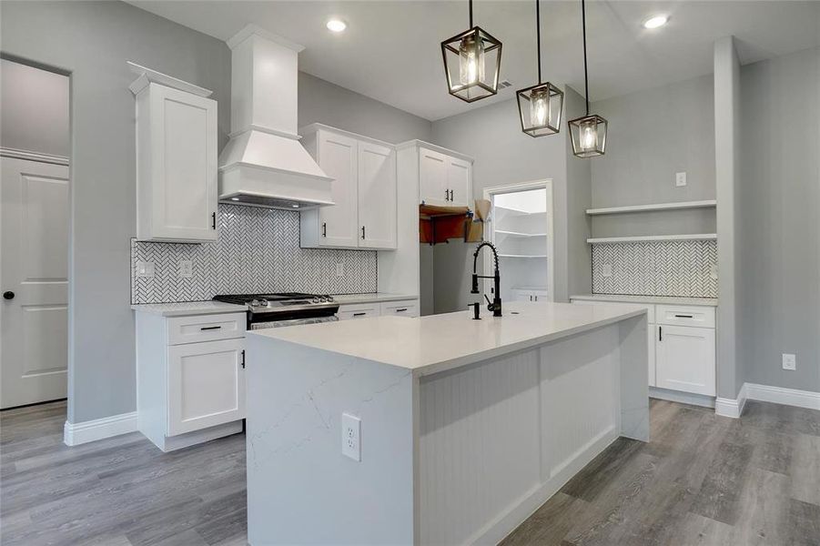 Kitchen with light wood-type flooring, white cabinets, stainless steel range with gas cooktop, backsplash, and custom exhaust hood