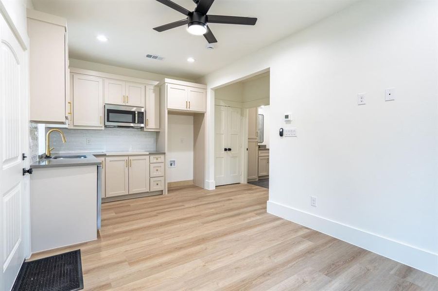 Kitchen with white cabinets, decorative backsplash, sink, ceiling fan, and light wood-type flooring