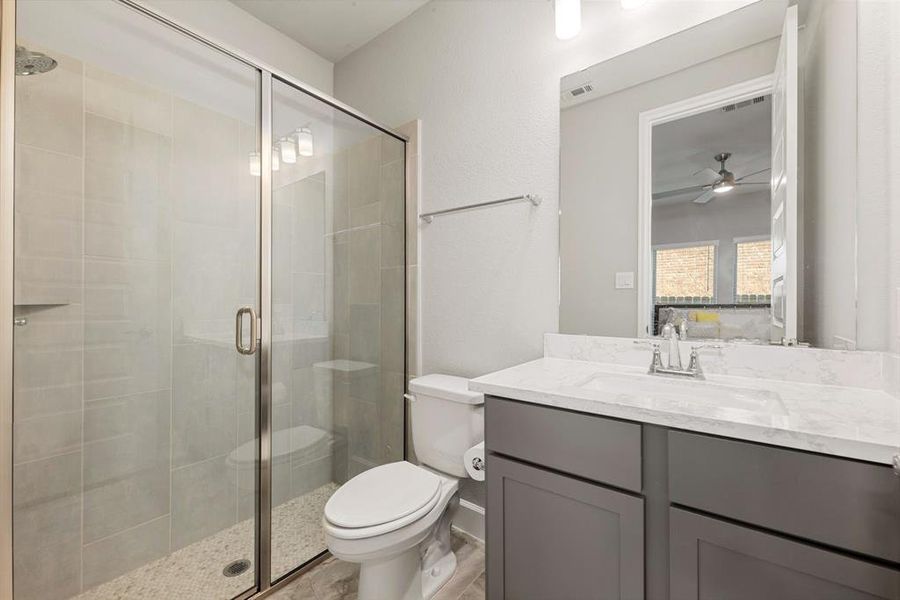 Secondary bathroom located just off the guest room, features light countertops and cabinets, custom paint, large walk in shower with tile surround, mirror, tile floors, sleek fixtures and modern finishes, plenty of space to accommodate any visiting family or guests.