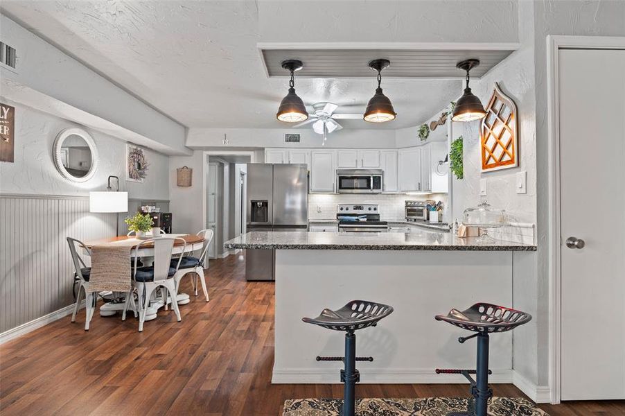 Kitchen with white cabinetry, pendant lighting, dark hardwood / wood-style floors, appliances with stainless steel finishes, and kitchen peninsula