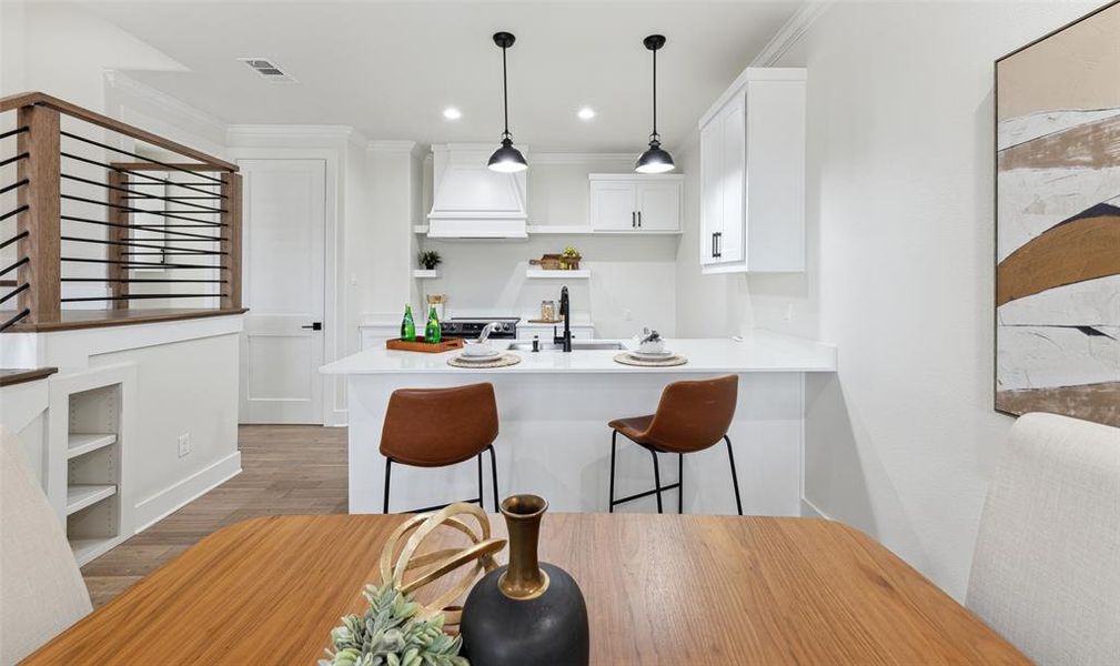 Kitchen with white cabinets, hardwood / wood-style flooring, custom range hood, and ornamental molding