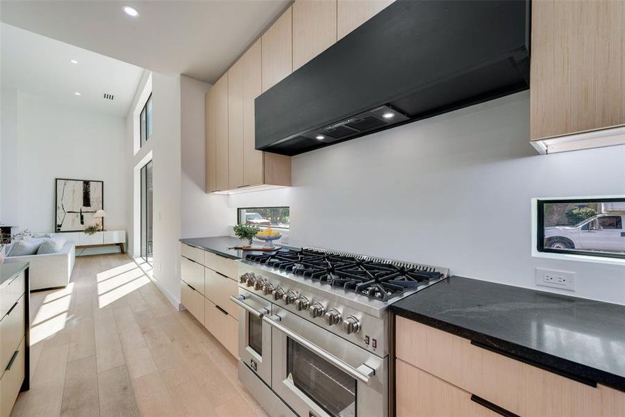 Kitchen with double oven range, light hardwood / wood-style floors, light brown cabinetry, and range hood