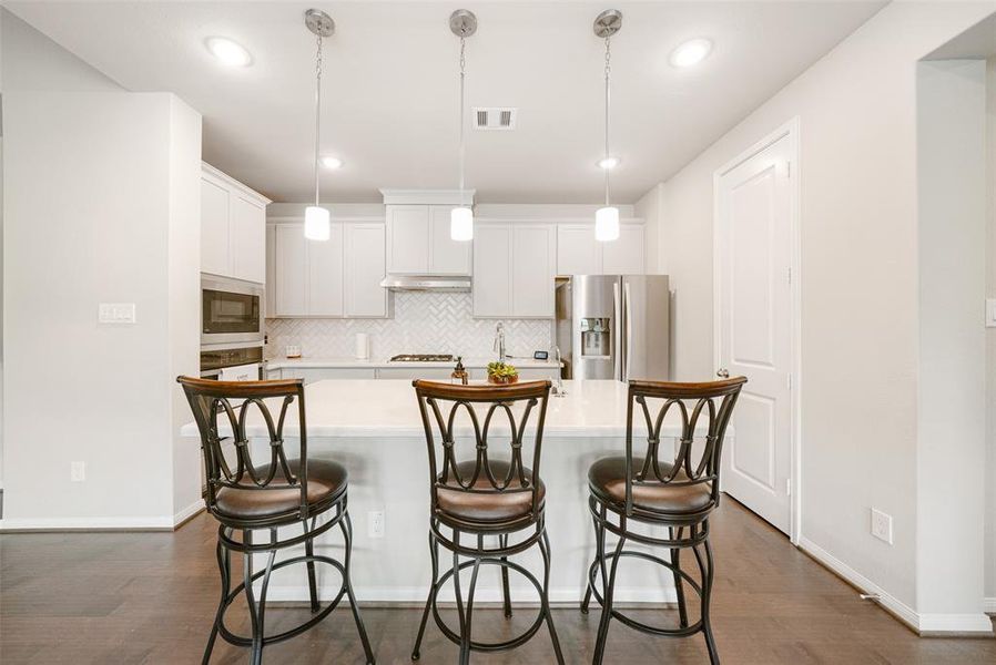 What a great modern kitchen with ample cabinetry, stainless steel appliances, and a breakfast bar with pendant lighting.