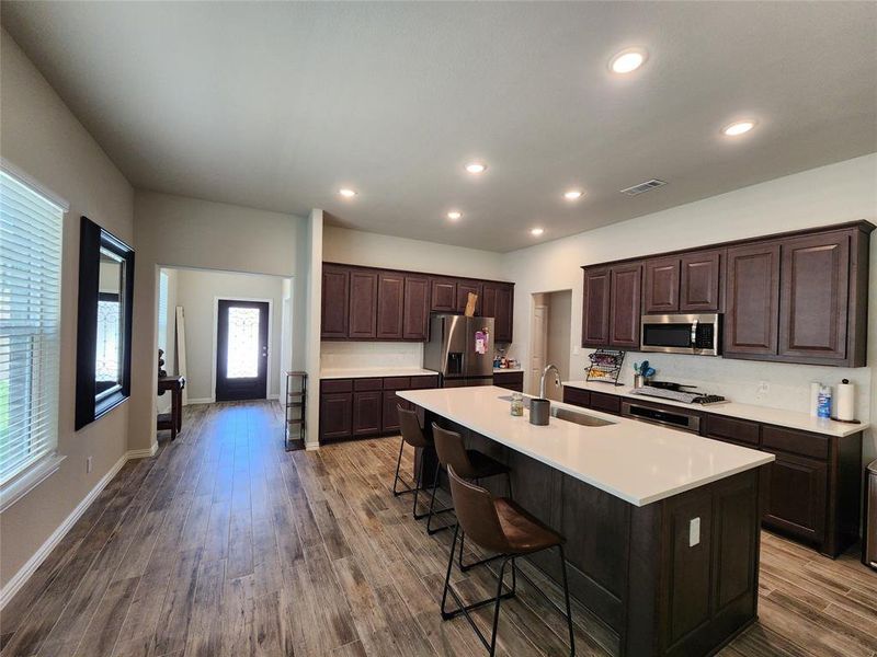 Kitchen with a kitchen island with sink, hardwood / wood-style flooring, sink, appliances with stainless steel finishes, and a kitchen breakfast bar