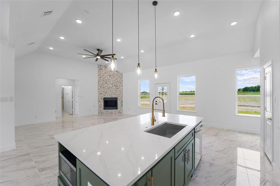 Kitchen featuring a center island with sink, a large fireplace, sink, light tile flooring, and ceiling fan