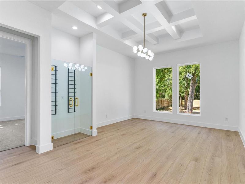 Empty room with coffered ceiling, beamed ceiling, light wood-type flooring, and a chandelier