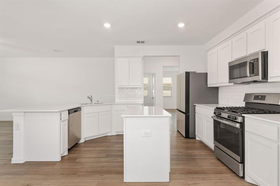 Kitchen with backsplash, light hardwood / wood-style floors, a kitchen island, and appliances with stainless steel finishes