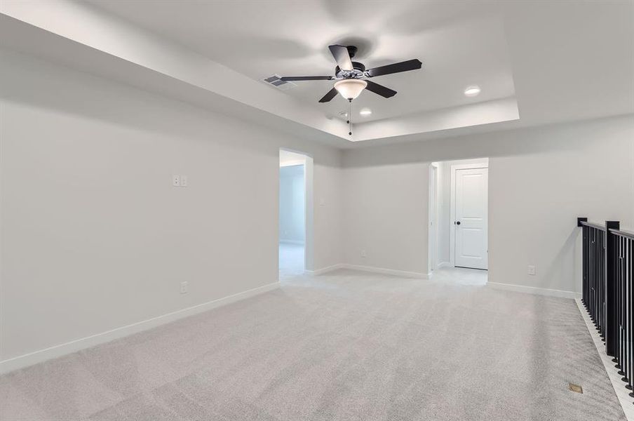 Empty room featuring light colored carpet, a raised ceiling, and ceiling fan