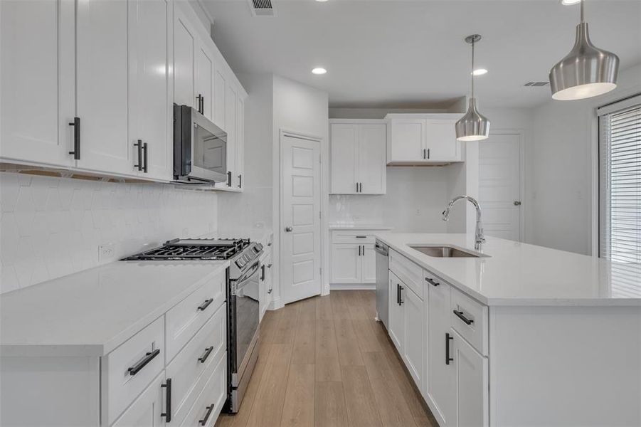 Kitchen with stainless steel appliances, tasteful backsplash, white cabinetry, light wood-type flooring, and sink