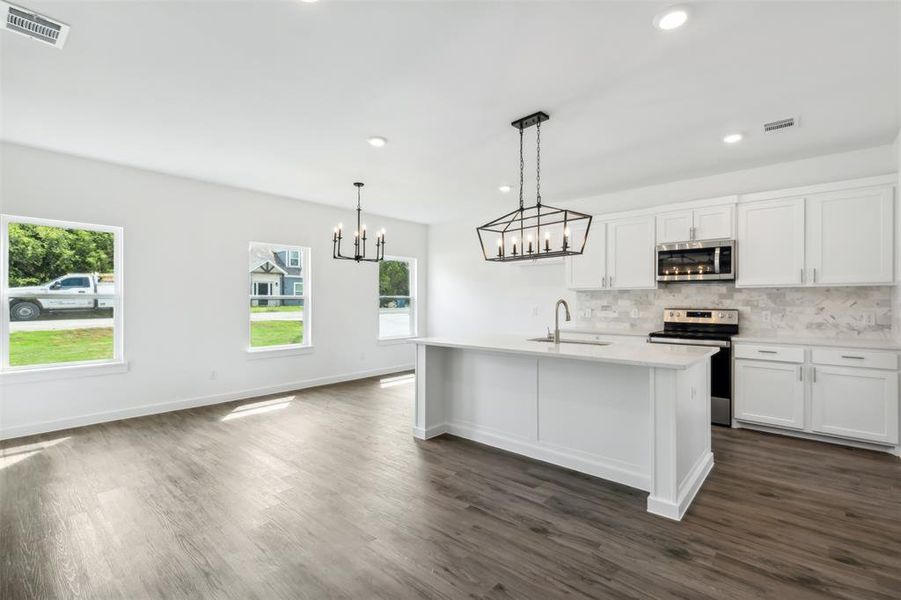 Kitchen with decorative light fixtures, dark hardwood / wood-style flooring, a center island with sink, appliances with stainless steel finishes, and sink