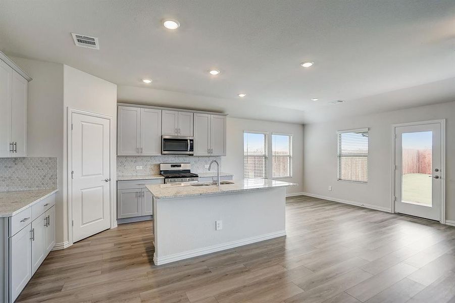 Kitchen with light stone countertops, stainless steel appliances, light wood-type flooring, and sink