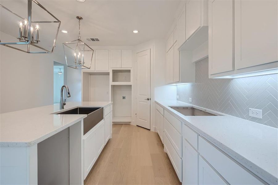 Kitchen featuring pendant lighting, sink, a center island with sink, white cabinetry, and light hardwood / wood-style floors