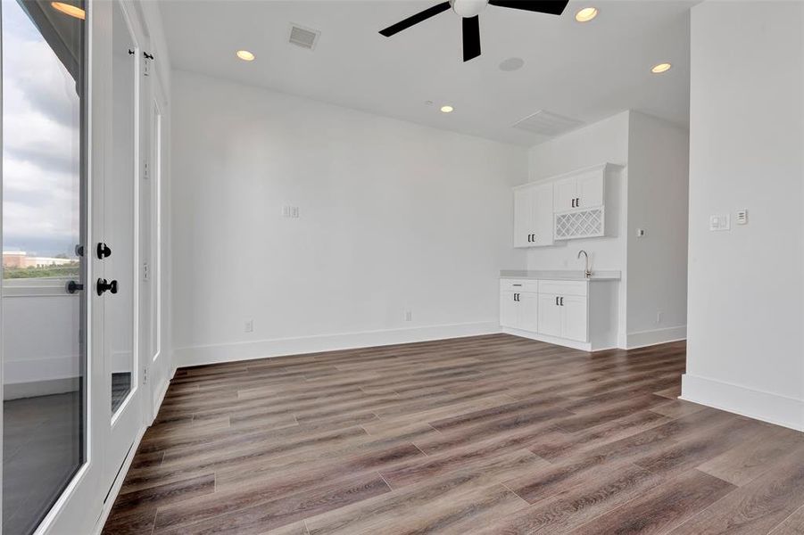 The game room on the fourth floor includes a single sink and several cabinets for storage, complemented by large windows and doors that lead to the balcony, creating a bright and inviting space.