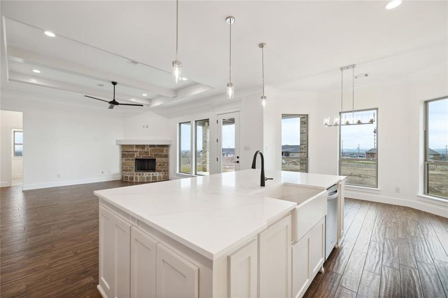 Kitchen with dark wood-type flooring, a healthy amount of sunlight, an island with sink, and a stone fireplace