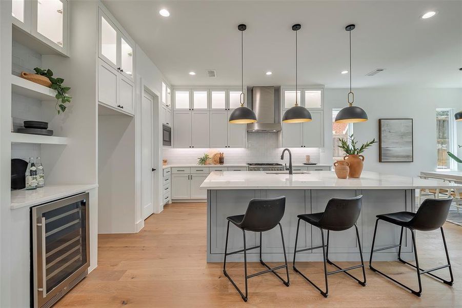 Kitchen with wall chimney range hood, light hardwood / wood-style flooring, beverage cooler, a wealth of natural light, and white cabinets